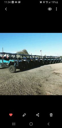 Long row of side-by-side UTVs parked on a gravel lot under a clear blue sky, ready for off-road desert tours