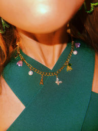 Close-up of a neckline in a green ribbed V-top wearing a gold charm chain necklace with an 'A' initial, pearl, butterfly and flower charms — fashion accessory detail