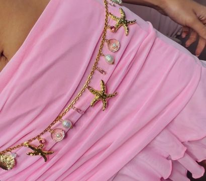 Close-up of pink ruffled sarong tied at the waist with a gold charm belt featuring starfish, shell charms and pearl beads — beachy summer outfit detail.