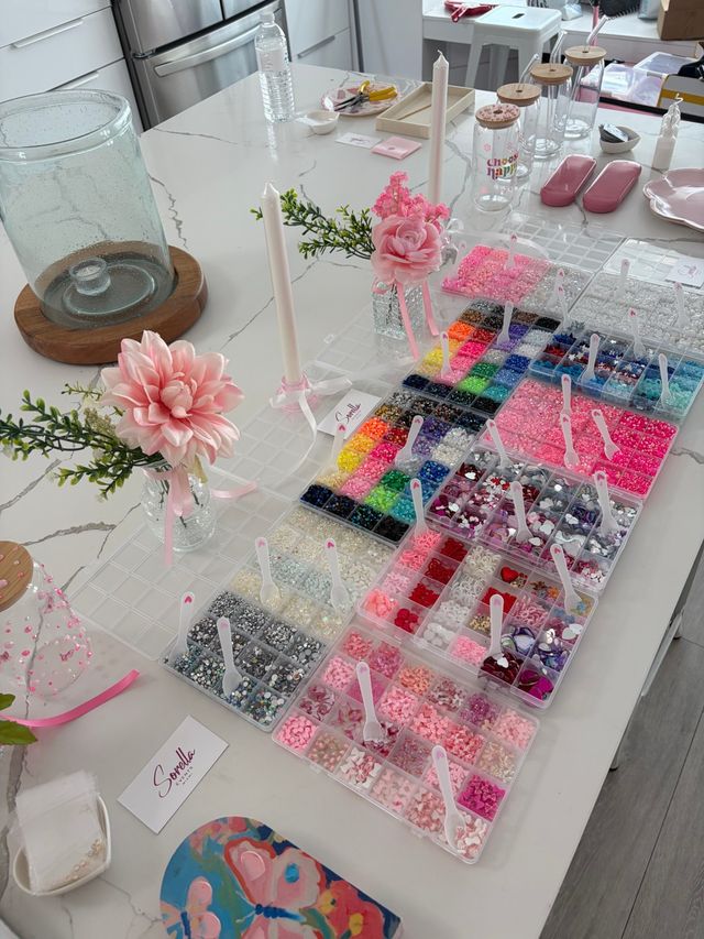 DIY craft station on white marble kitchen island with organized trays of colorful beads, sequins and rhinestones, pink floral accents and candles