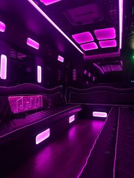 Luxury party bus interior with vibrant purple LED lighting, quilted leather bench seating, mirrored ceiling panels and wood-look floor creating a lounge-style nightlife atmosphere