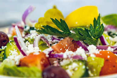 Close-up of a vibrant Greek salad with juicy tomatoes, cucumber slices, red onion, Kalamata olives, crumbled feta, a lemon wedge and parsley on crisp lettuce