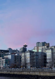 Pastel pink-blue sunset over Seattle waterfront, Space Needle peeking above modern riverside apartment buildings.