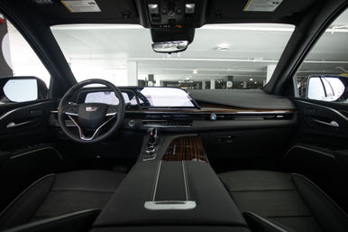 Sleek luxury SUV interior parked in an indoor parking garage, showing leather seats, leather-wrapped steering wheel, wide digital dashboard touchscreen, wood-trim center console and chrome gear shifter.