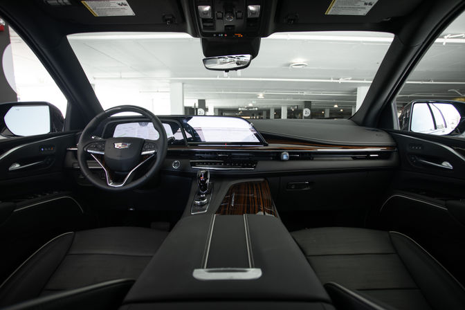 Sleek luxury SUV interior parked in an indoor parking garage, showing leather seats, leather-wrapped steering wheel, wide digital dashboard touchscreen, wood-trim center console and chrome gear shifter.