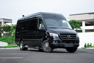 Black Mercedes passenger van parked in an urban office complex parking lot, front three-quarter view