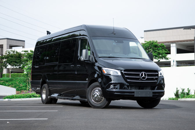 Black Mercedes passenger van parked in an urban office complex parking lot, front three-quarter view
