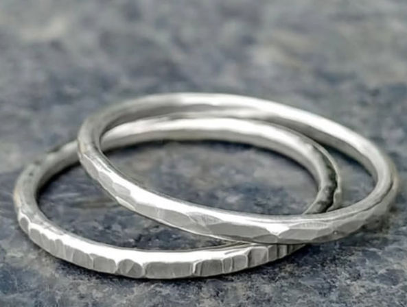 Handmade hammered silver stacking rings with a textured finish resting on a gray stone surface