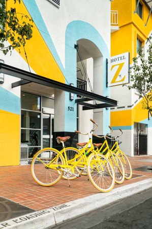 Bright yellow bicycles parked on a brick sidewalk outside a colorful hotel entrance with a blue arch and bold yellow-and-blue mural