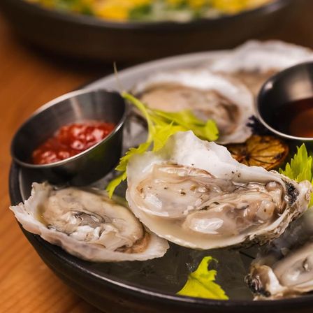 Raw oysters on the half shell on crushed ice with cocktail sauce, lemon and greens — a briny seafood platter at a coastal restaurant.