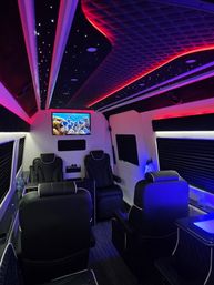Luxury van interior with quilted black leather recliners, starry fiber-optic ceiling and red-blue LED accent lighting, wall-mounted TV showing a colorful coral reef — upscale mobile lounge.