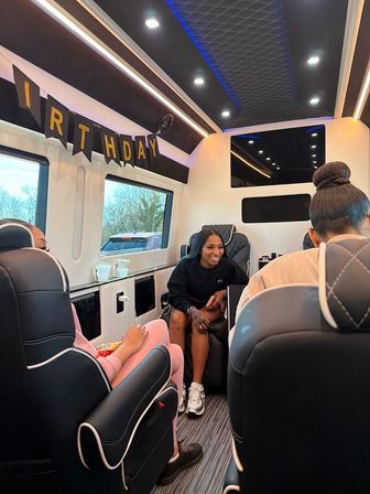 Birthday celebration inside a luxury party van: smiling friends seated on quilted leather seats with windows and blue LED ceiling lights.