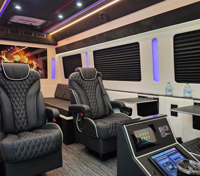 Sleek luxury van interior with quilted black leather captain chairs, ambient multicolor LED ceiling lights, touchscreen control panels and cup holder — modern executive shuttle cabin