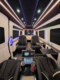 Luxurious VIP shuttle van interior with quilted black leather captain seats, LED ambient ceiling lights, fold-out trays, touchscreen controls, cup holders and rear entertainment screen