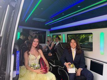 Prom group of young people in formal dresses and suits inside a luxury limo with quilted black leather seats, neon green-blue LED ambient lighting, and visible corsages and boutonnières.