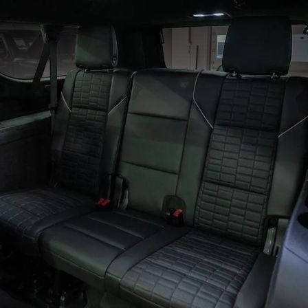 Sleek black leather rear car bench seat with quilted upholstery, three headrests, seatbelts and red buckle latches in a dimly lit vehicle interior.