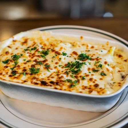 Creamy baked macaroni and cheese with golden-brown broiled cheese topping and chopped parsley in a white ceramic baking dish on a striped plate