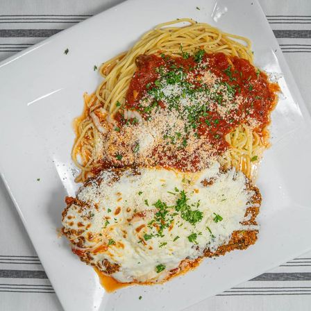 Top-down shot of classic chicken Parmesan—crispy breaded cutlet with melted mozzarella and parsley—served with spaghetti marinara and grated Parmesan on a white plate.