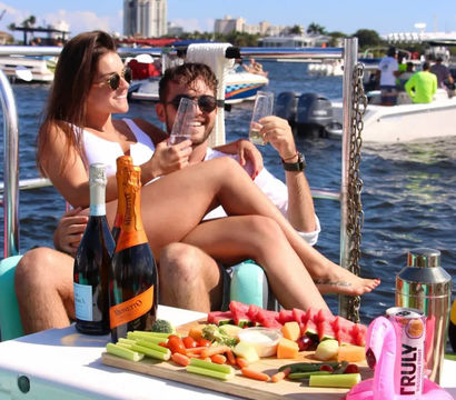Couple toasting with champagne on a sunny boat party at a busy marina, picnic board of fruit, veggies and bottles in the foreground