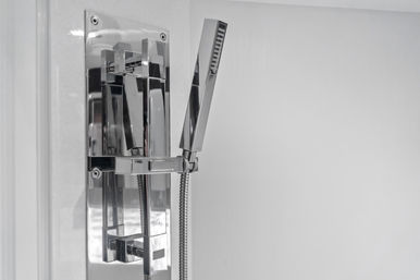 Close-up of a sleek chrome handheld showerhead and rectangular lever controls mounted on a white bathroom wall, modern minimalist bathroom fixture.