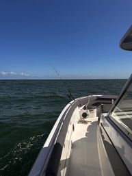 White fishing boat starboard deck with a rod cast into deep green open ocean under a clear blue sky