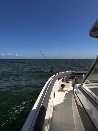White fishing boat starboard deck with a rod cast into deep green open ocean under a clear blue sky