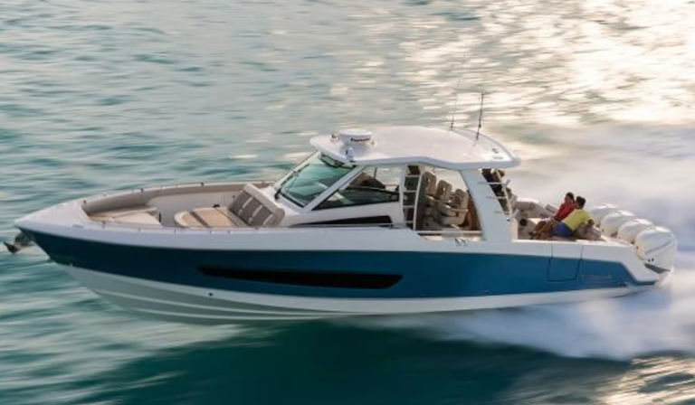 Sleek blue-and-white powerboat racing across turquoise coastal waters with passengers on the stern and a frothy wake trailing in bright sunlight.