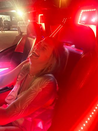 Joyful person laughing in a red LED-lit car interior at night, reclining in a leather seat on a lively night out.