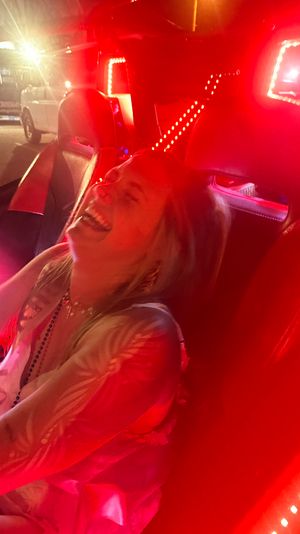 Joyful person laughing in a red LED-lit car interior at night, reclining in a leather seat on a lively night out.