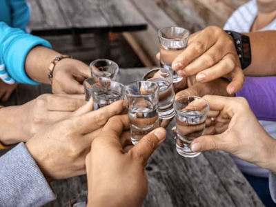 Friends clinking clear shot glasses in a cheerful toast over a rustic wooden outdoor table