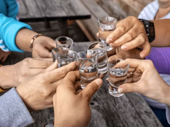 Friends clinking clear shot glasses in a cheerful toast over a rustic wooden outdoor table