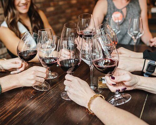 Group of people clinking stemmed glasses of red wine in a cheerful toast at a wooden table during a casual wine tasting