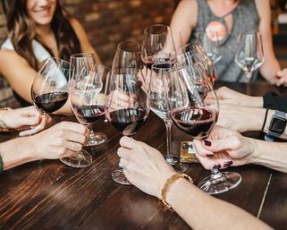Group of people clinking stemmed glasses of red wine in a cheerful toast at a wooden table during a casual wine tasting