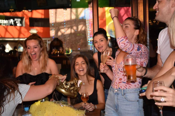 Lively group of friends laughing and cheering with champagne flutes and a beer at an indoor bar during a birthday-style celebration