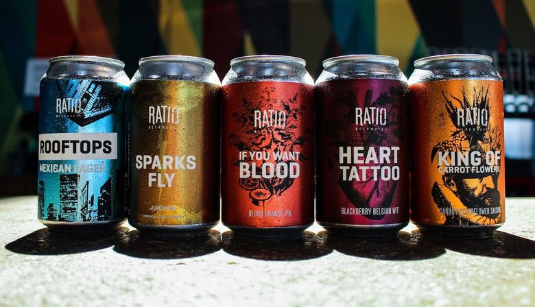 Five colorful craft beer cans lined up on a sunlit counter, bold labels and vibrant artwork highlighting Mexican lager, juicy IPA, blood orange IPA, blackberry Belgian wit and carrot-flower saison.