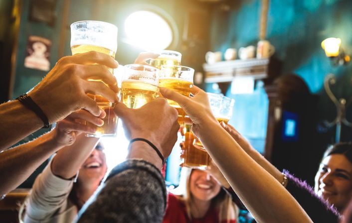 Close-up of friends clinking beer glasses in a cozy pub, golden light and smiling faces