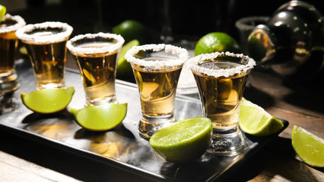 Golden tequila shots in salt-rimmed glasses with bright lime wedges arranged on a metal tray at a bar