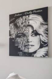 Black-and-white canvas wall art showing a glamorous blonde female portrait split with bold stacked song lyrics, hung above a bed on a light gray bedroom wall