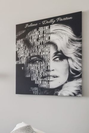 Black-and-white canvas wall art showing a glamorous blonde female portrait split with bold stacked song lyrics, hung above a bed on a light gray bedroom wall