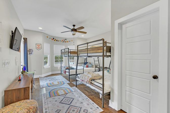 Bright kids' bedroom in a family home with two metal twin bunk beds, colorful rugs and bunting, ceiling fan and wall-mounted TV.