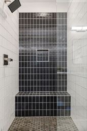 Sleek modern bathroom shower with glass enclosure, hexagon stone floor, white square wall tiles, a floor-to-ceiling black wavy-tile accent wall with built-in niche and bench, and a square rain showerhead.