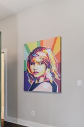 Vibrant geometric pop-art canvas portrait of a woman with rainbow rays, hanging on a light-gray wall in a modern home hallway
