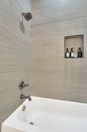 Sleek contemporary residential shower-tub with light beige horizontal tile, brushed nickel showerhead and tub faucet, and a recessed niche holding black pump bottles