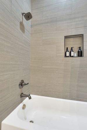Sleek contemporary residential shower-tub with light beige horizontal tile, brushed nickel showerhead and tub faucet, and a recessed niche holding black pump bottles