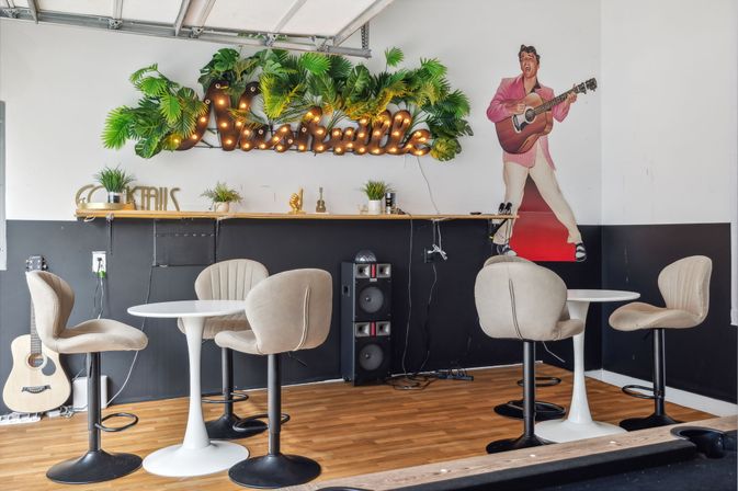 Cozy Nashville-themed music café interior with round white tables, beige swivel chairs, acoustic guitar, speaker stack, illuminated marquee “Nashville” sign with tropical greenery, and a guitar-playing singer mural.