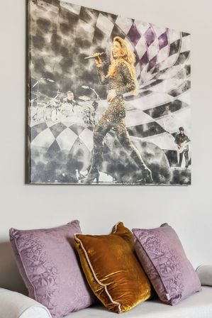 Modern living room with a large canvas print of a female singer performing on stage, mounted above a sofa dressed with lilac patterned throw pillows and a golden velvet cushion.