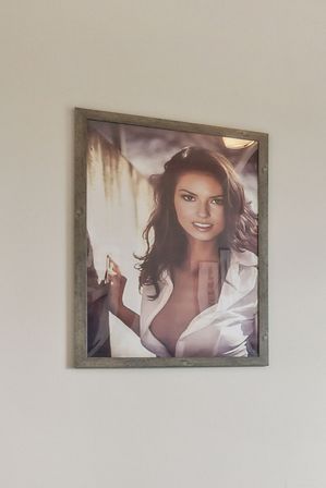 Chic framed portrait poster of a smiling woman in an open white shirt displayed as interior wall decor on a plain beige wall.