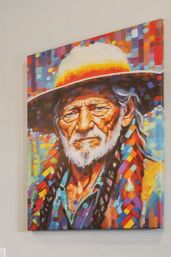 Vibrant mosaic-style canvas portrait of a weathered bearded man wearing a wide-brim hat and colorful braided scarf, mounted on a neutral indoor wall.