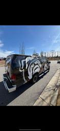 Black cargo van with a bold white-and-red bulldog mural parked at a suburban street curb beside an empty lot, leafless trees and a clear blue sky overhead.