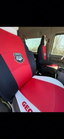 Truck interior with custom red, black and white seat covers featuring a bold bulldog emblem and partial "GEO" lettering on the front bench and captain’s seat